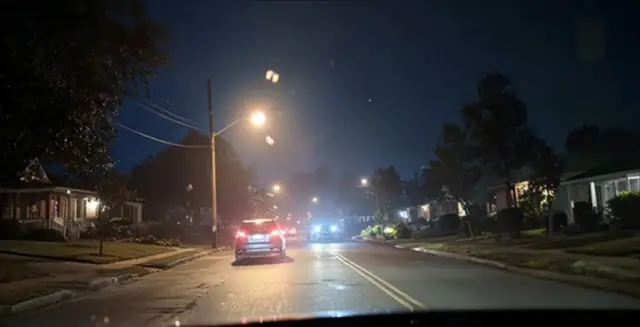 Suburban street at night lit by streetlights and car headlights